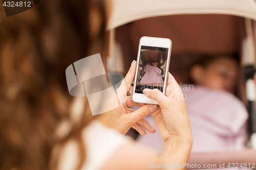 Image of mother with smartphone and stroller at park