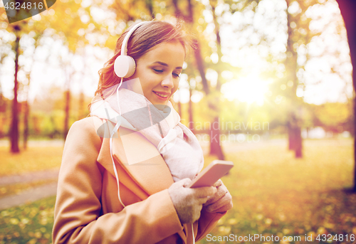Image of woman with smartphone and earphones in autumn park