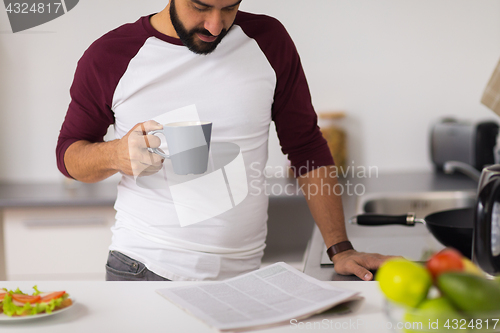 Image of man with coffee reading newspaper at home kitchen