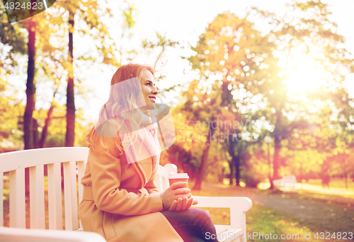 Image of happy young woman drinking coffee in autumn park