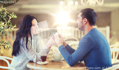 Image of happy couple with tea holding hands at restaurant