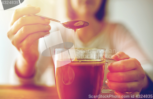 Image of close up of woman adding honey to tea with lemon