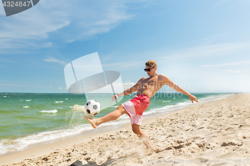 Image of young man with ball playing soccer on beach