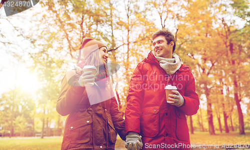 Image of happy couple with coffee walking in autumn park