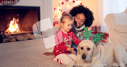 Image of Mom and daughter in sweaters play with pet dog