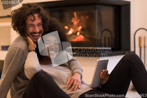 Image of multiethnic couple using tablet computer on the floor