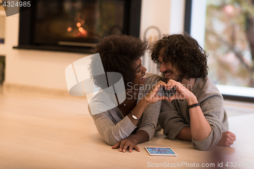 Image of multiethnic couple showing a heart with their hands on the floor