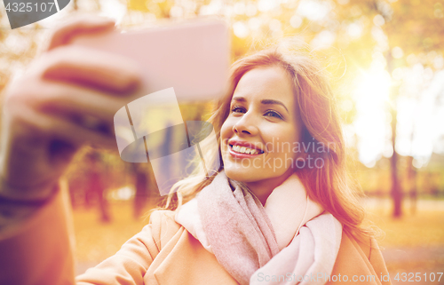 Image of woman taking selfie by smartphone in autumn park