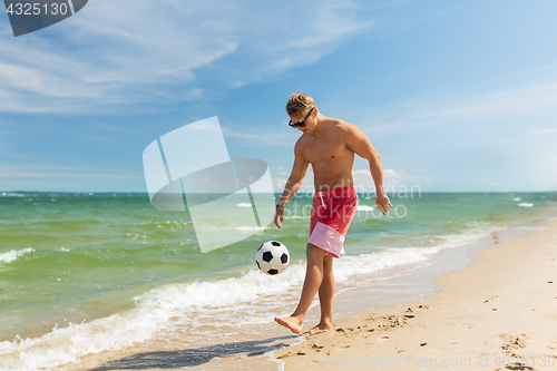 Image of young man with ball playing soccer on beach