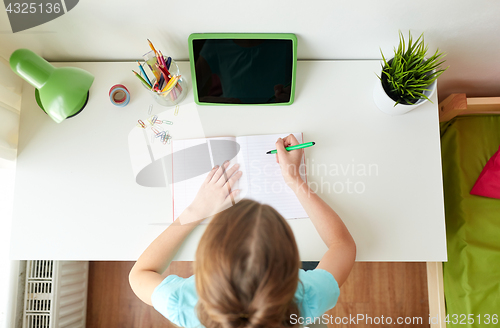 Image of girl with tablet pc writing to notebook at home