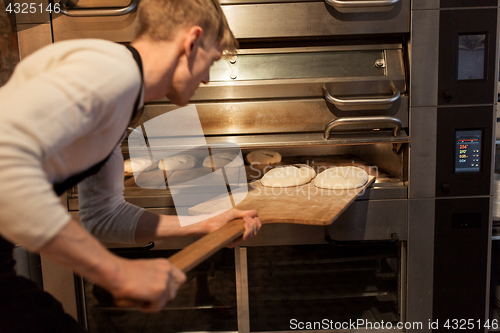 Image of baker putting dough into bread oven at bakery