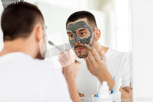 Image of young man applying clay mask to face at bathroom