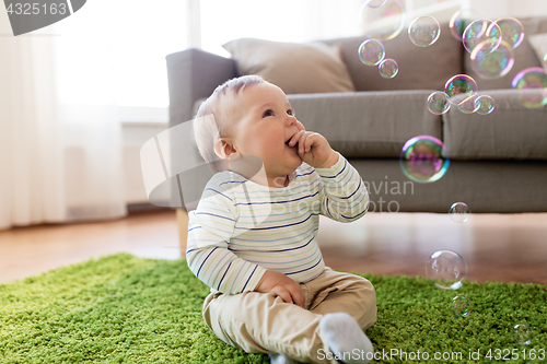 Image of baby boy playing with soap bubbles at home