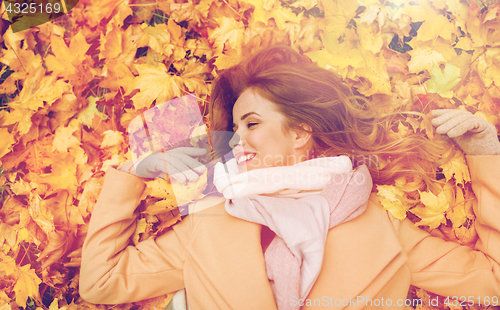 Image of beautiful happy woman lying on autumn leaves