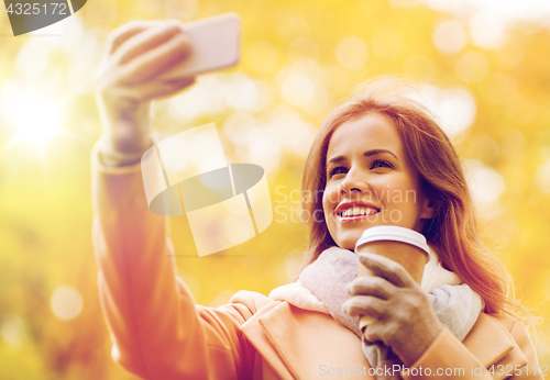 Image of woman taking selfie by smartphone in autumn park