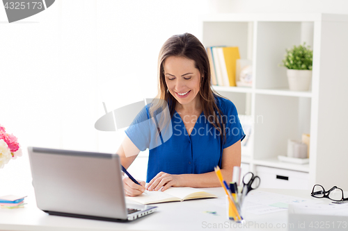 Image of happy woman writing to notebook at office