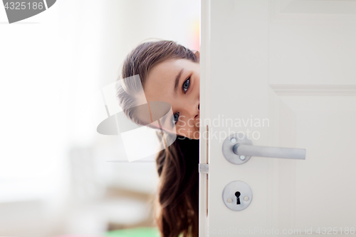 Image of happy smiling beautiful girl behind door at home