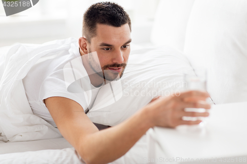 Image of man in bed with glass of water at home