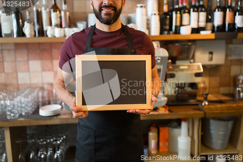 Image of happy man or waiter with blank blackboard at bar