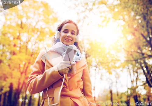 Image of woman with smartphone and earphones in autumn park