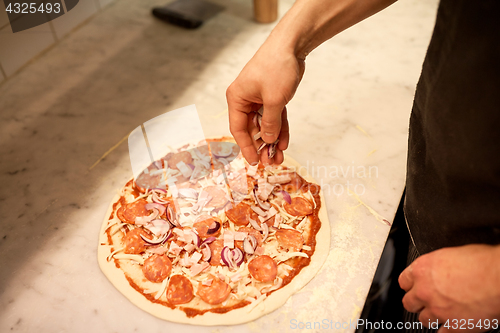 Image of cook adding onion to salami pizza at pizzeria