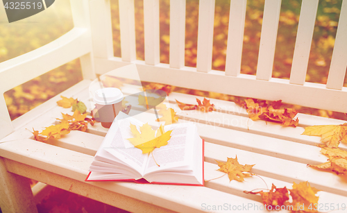 Image of open book and coffee cup on bench in autumn park