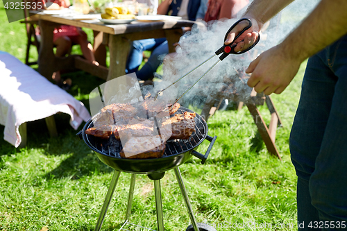 Image of man cooking meat on barbecue grill at summer party