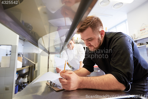Image of chef and cook with lists or bills at kitchen