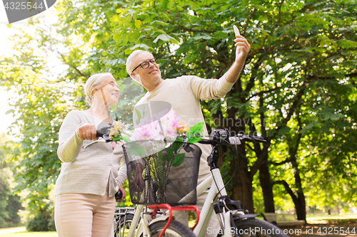 Image of senior couple with bicycles taking selfie at park