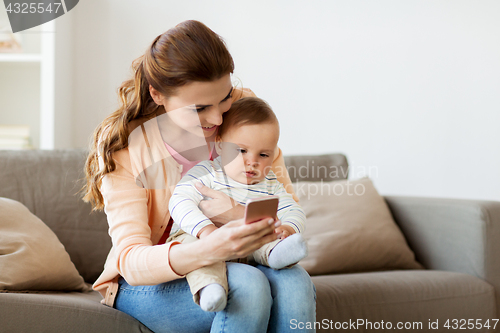 Image of happy mother with baby and smartphone at home