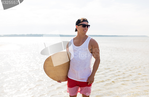 Image of happy young man with skimboard on summer beach