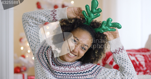 Image of Playful young woman wearing green reindeer antlers