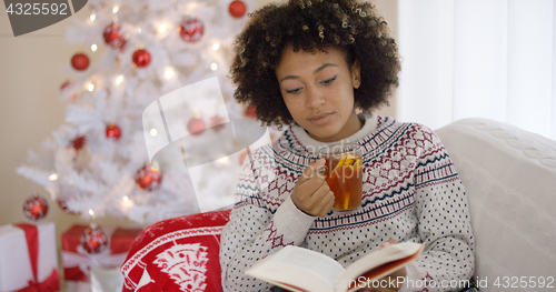 Image of Woman reading a book in front of a Christmas tree