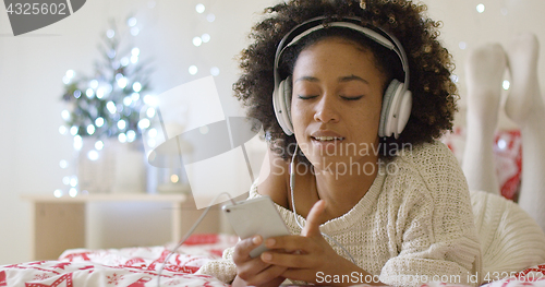 Image of Lady in white sweater on bed listening to music