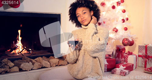 Image of Pretty woman holds wine glass beside fireplace