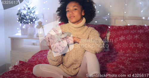 Image of Single woman holding Christmas gift in bed