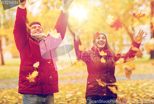 Image of happy young couple throwing autumn leaves in park