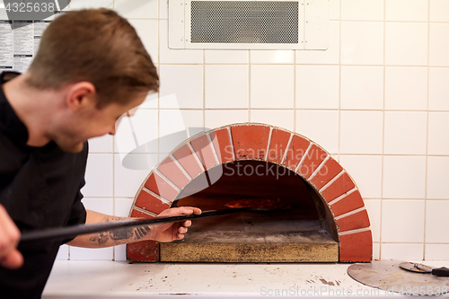 Image of man with peel placing pizza to oven at pizzeria