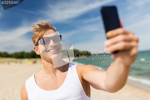 Image of man with smartphone taking selfie on summer beach