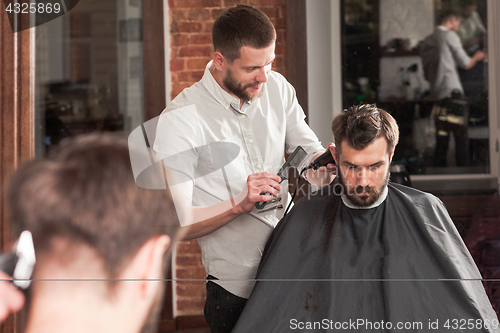 Image of Young handsome barber making haircut of attractive man in barbershop