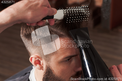 Image of The hands of barber making haircut to young man in barbershop