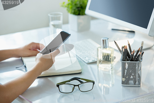 Image of Close-up of female hands using smart phone while working on computer at modern office interior