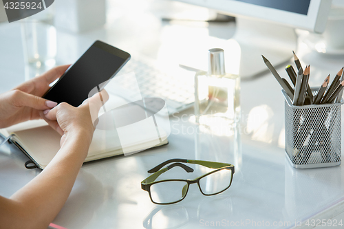 Image of Close-up of female hands using smart phone while working on computer at modern office interior