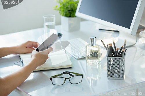 Image of Close-up of female hands using smart phone while working on computer at modern office interior