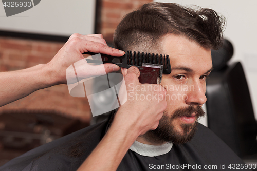 Image of The hands of barber making haircut to young man in barbershop