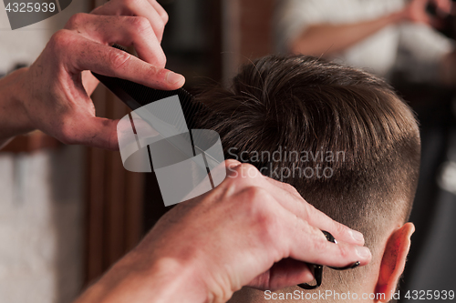 Image of The hands of barber making haircut to young man in barbershop