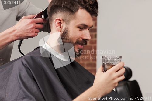 Image of The hands of barber making haircut to young man in barbershop