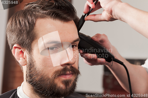 Image of The hands of barber making haircut to young man in barbershop