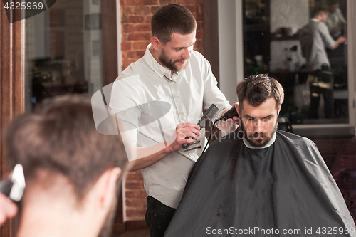 Image of Young handsome barber making haircut of attractive man in barbershop