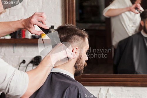 Image of The hands of barber making haircut to young man in barbershop